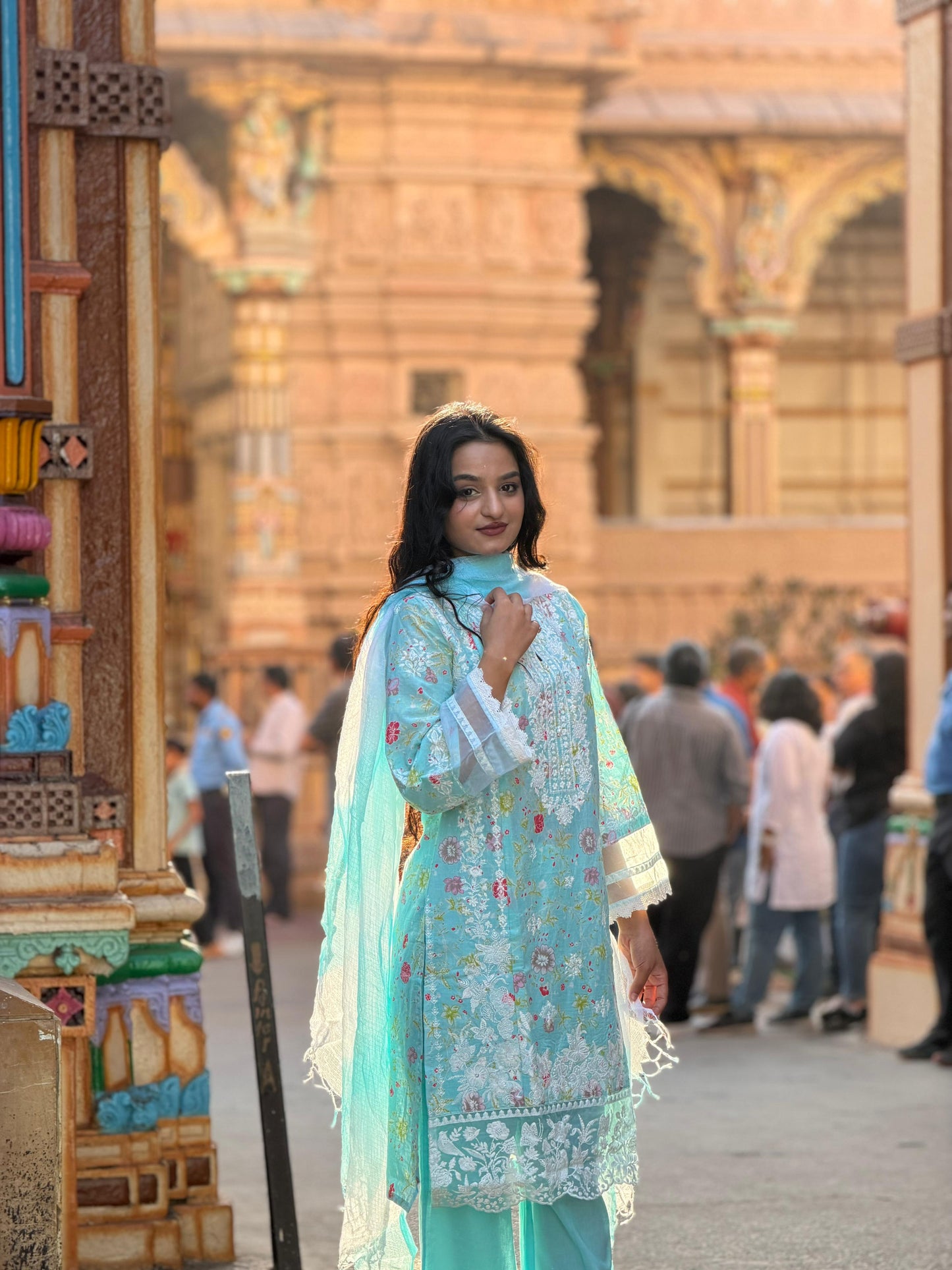 Woman in a light blue traditional outfit standing in front of a decorative wall.